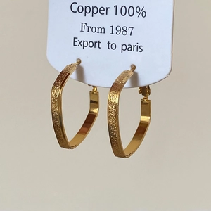 Detailed macro view of gold heart and triangle copper earrings with matte texture finish