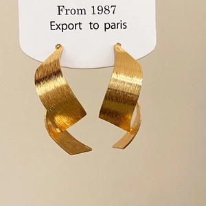 Close-up of golden brushed metal stud earrings in a twisted ribbon design on display card