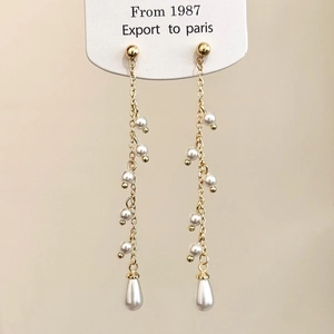 Macro detail of long gold pearl tassel earrings with elegant teardrop pendant dangles