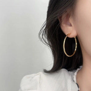 Boucles d'oreilles créoles dorées avec motif texturé portées par un mannequin élégant