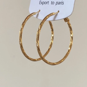 Détail macro de créoles dorées présentant une texture tissée en spirale sophistiquée