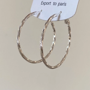 Détail de créoles géométriques argentées avec motif en spirale texturé sur carte blanche