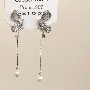 Detailed view of silver bow drop earrings with long chain tassels and white pearls