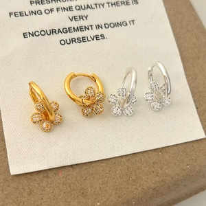 Gold and silver flower hoop earrings with white zircon stones on a paper background