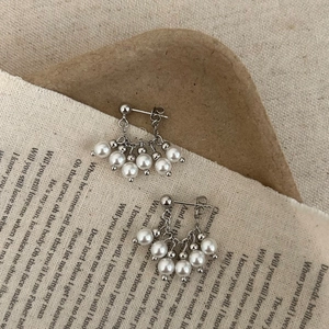 Dettaglio macro di orecchini vintage con perle e catene d'argento su sfondo di carta rustica