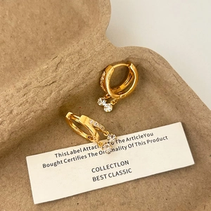 Détail de boucles d'oreilles créoles dorées avec cristaux de zircon sur une carte décor