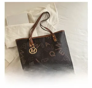 Detail of monogram printed tote bag with brown leather handles and gold 'M' charm