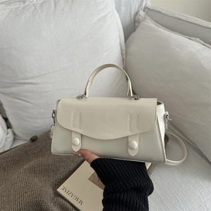 Stylish cream crossbody bag with top handle and vertical stitching detail on sofa