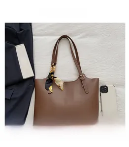 Brown tote bag detail with decorative scarf, smartphone and notebook on white fabric