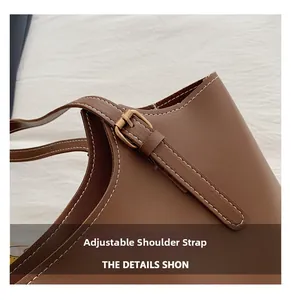 Detail of adjustable shoulder strap on brown leather tote with white stitching and gold buckle