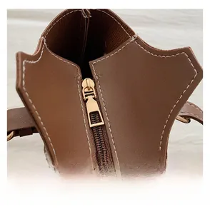 Detailed close-up of brown leather bag featuring contrast white stitching and gold zipper