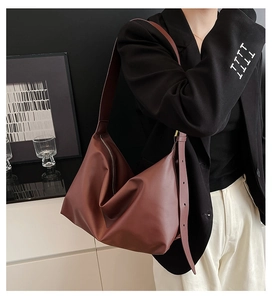 Deep burgundy leather tote bag with wide strap worn by model in a minimalist setting