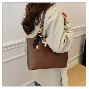 Brown leather tote bag with decorative silk scarf accessory shown on model shoulder
