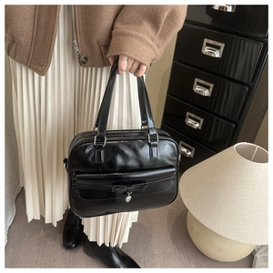 Detalle de bolso tote negro con lazo y colgante de corazón en una escena de estilo de vida