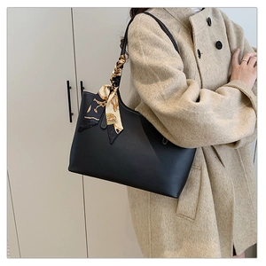 Close-up of black leather tote bag with elegant chain print silk scarf detail on handle