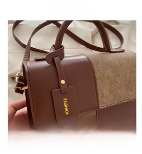 Detailaufnahme der Kontrastnähte und des goldenen Logo-Anhängers der braunen Tasche