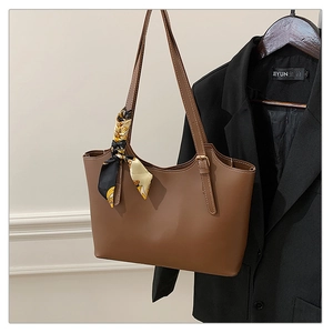 Brown leather tote bag featuring elegant patterned silk scarf on strap with black suit