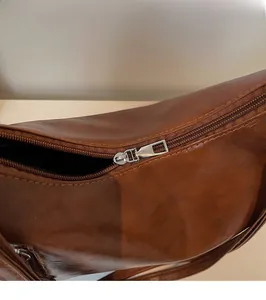 Close-up of smooth silver metal zipper on a brown vintage leather shoulder bag