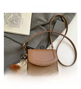 Detail of brown litchi pattern leather crossbody bag with quirky plush monster charm