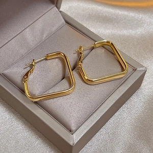 Boucles d'oreilles carrées géométriques dorées posées sur un fond en tissu de soie