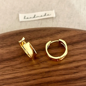 Macro view of gold irregular wide hoop earrings on a textured wooden and linen display