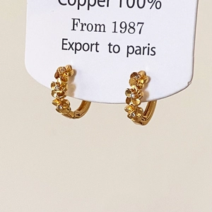 Gros plan de boucles d'oreilles en cuivre doré avec petites fleurs 3D incrustées de zircon
