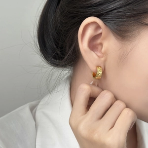 Golden hoop earrings with koi fish scale texture worn by a model in a minimalist style