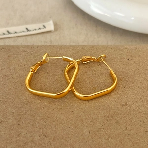 Détail de boucles d'oreilles créoles carrées en métal doré sur fond de papier naturel