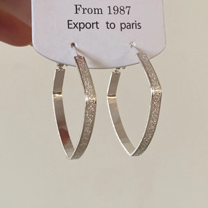 Macro detail of geometric V-shaped silver hoop earrings with polished and frosted finish