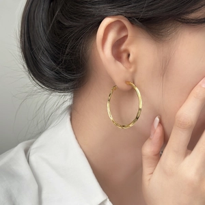 Fashionable gold hoop earrings with twisted texture worn by a model on a white shirt