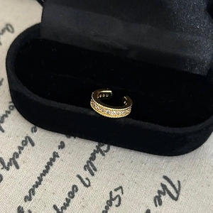 Detail of gold ear cuff with milgrain edges and white crystals in a jewelry box
