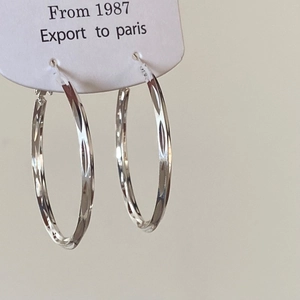 Close-up of silver hoop earrings with diamond-cut texture on a white jewelry tag