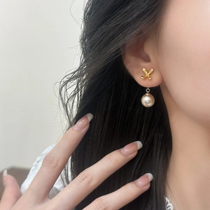 Elegant gold bow and pearl drop earrings for women shown on a model in soft light