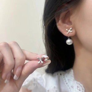 Close-up of silver star earrings with round white pearl drop pendant on model
