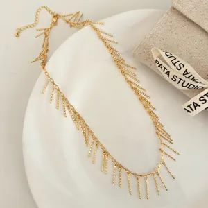 Gros plan d'un collier à franges dorées avec pendentifs barres texturés sur un plateau