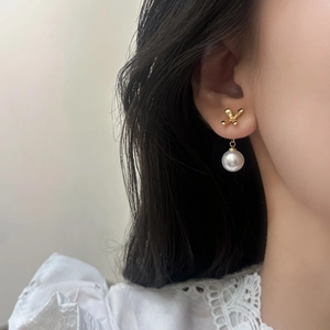 Elegant gold bow stud earrings with round white pearl drop on female model wearing lace