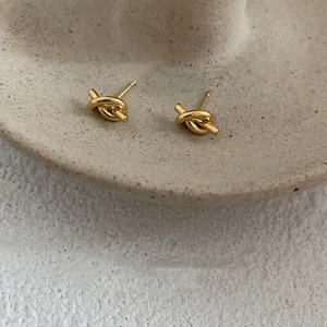 Close-up of polished knot-shaped gold earrings on a textured stone display tray