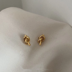 Detail of elegant 18K gold-plated knot stud earrings on a textured light grey display