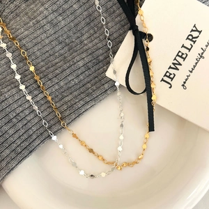 Minimalist gold and silver necklaces featuring heart-shaped links on a white plate