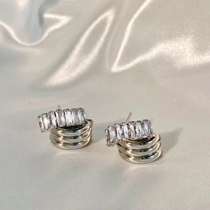 Detailed close-up of layered gold stud earrings with rectangular zircon on silk background