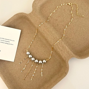 Detail view of a gold wave chain necklace with grey beads and flowing tassel fringe