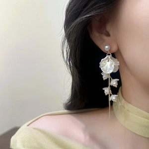 Detail of floral pearl tassel earrings featuring white petals and golden chain on model