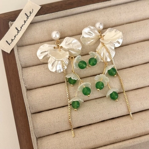 Detail of floral tassel earrings with white pearls and green beads on a velvet tray