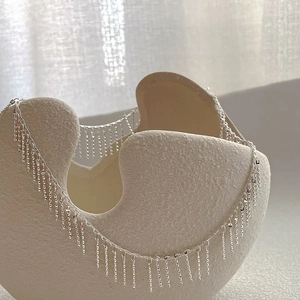 Detailopname van een zilveren kwastjesketting gedrapeerd op een beige keramieken vaas