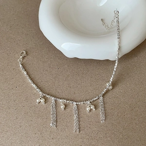 Detailed view of silver tassel necklace with pearls on a matte background