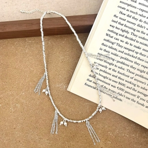 Macro detail of silver tassel necklace with white pearls on a rustic wood background