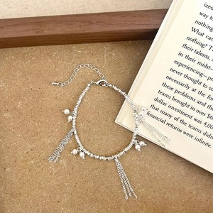 Detail of silver tassel necklace with pearl accents and adjustable chain on a rustic background
