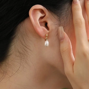 Elegant gold drop earring with natural freshwater pearl shown on model's ear