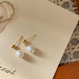 Elegant gold stud earrings with natural freshwater pearl pendants on beige texture background