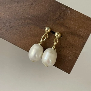Detail of baroque pearl drop earrings with gold wire wrap on a wooden display